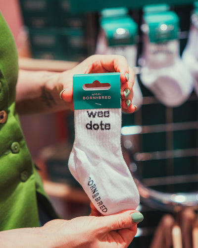 Person holding white baby socks with wee dote text on them